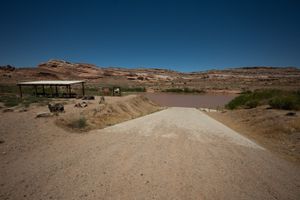 Gravel ramp running down to the muddy Colorado at Dewey Bridge, a shade pavilion and kiosk on the bench at left.