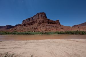 Wide sand beach at Hittle Bottom with the muddy Colorado beyond and a grey-capped red butte across the water.