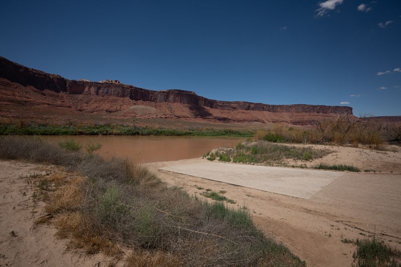 Concrete ramp apron running into the brown Colorado at Lower Onion Creek, a long red cliff line across the water.