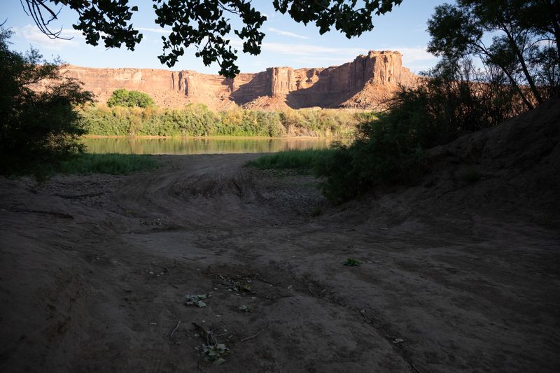 Dirt ramp dropping to the Green River at Mineral Bottom in early shade, the cliffs across the water still catching sun.