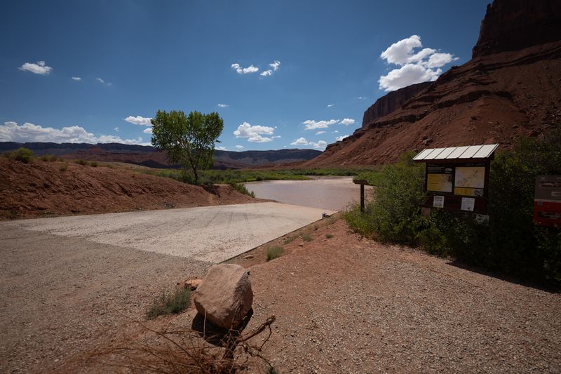 Concrete ramp and gravel apron at Rocky Rapid, a lone cottonwood at left and an information kiosk under the red cliff.