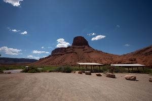 Two shade pavilions on the gravel flat at Rocky Rapid, a broad red butte rising behind and the river at left.