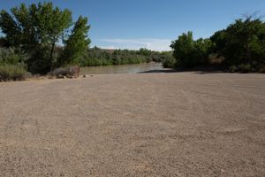 Broad gravel launch apron at Sand Island running down to the silty San Juan, cottonwoods on both banks.