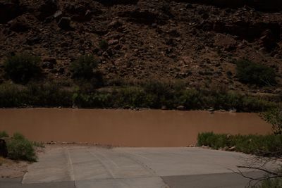Concrete ramp entering the muddy Colorado at Take Out Beach, a dark boulder slope rising on the far bank.