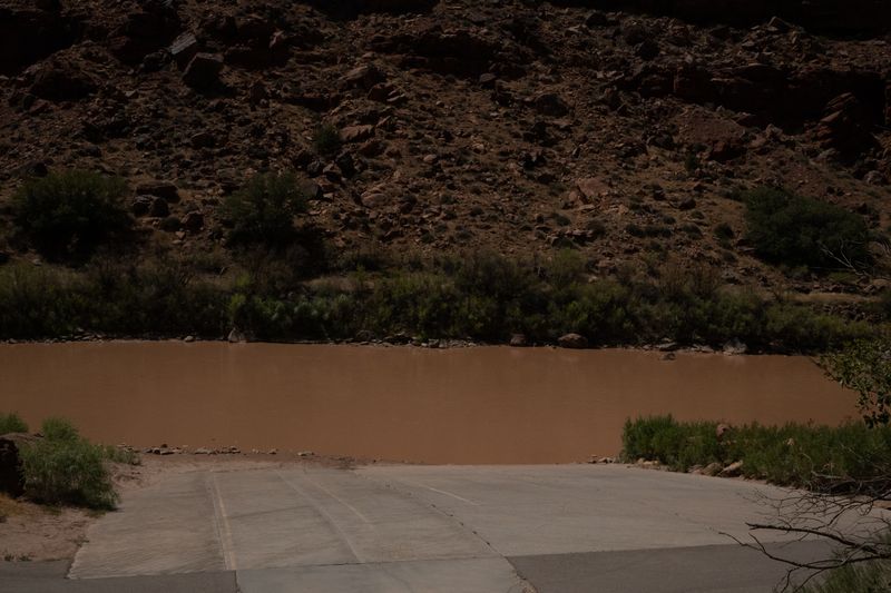 Concrete ramp entering the muddy Colorado at Take Out Beach, a dark boulder slope rising on the far bank.