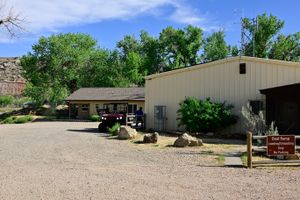 The Westwater ranger station buildings and gravel lot, with a red utility vehicle parked at a wooden fence, a radio mast above the cream metal building, tall green cottonwoods, and a brown Boat Ramp Loading and Unloading Only sign.