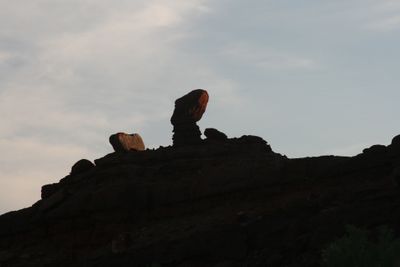 Silhouetted canyon rim at sunset, with the tilted cap of a balanced rock catching the last red light against a pale, hazy sky.