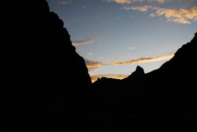 Canyon walls stand in black silhouette against a dusk sky with a few orange-lit clouds.