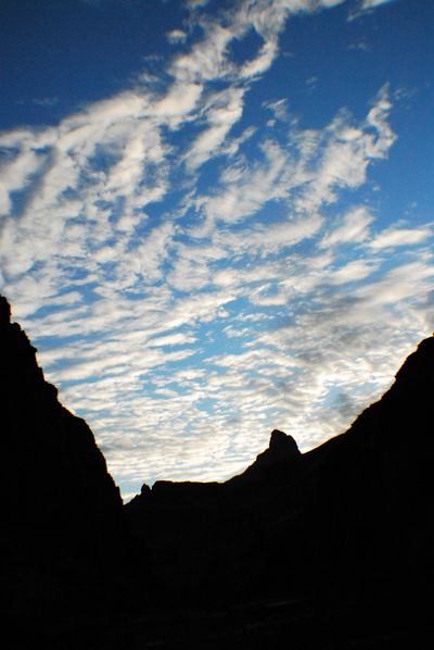 Rippled rows of small clouds fill a blue evening sky above canyon rims in black silhouette.