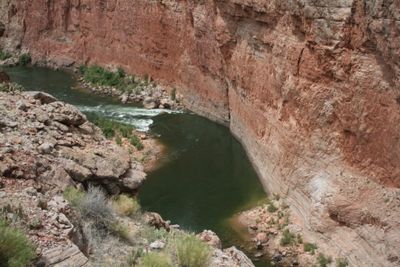 Seen from above, the green Colorado River curves beneath a sheer red wall as a small riffle breaks white mid-channel.
