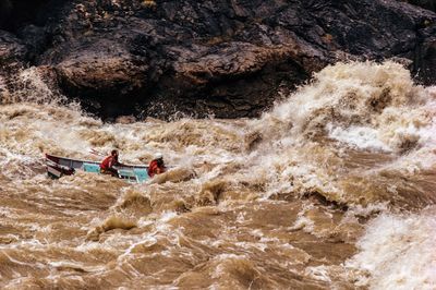 A dory with two boaters in red life jackets is nearly buried in huge muddy brown waves at Crystal Rapid on the Colorado River.