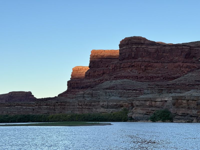Last light catches the caprock of a stepped red sandstone butte above a calm stretch of the Colorado River in Meander Canyon