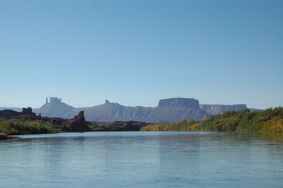 Calm stretch of the Colorado River on the Moab Daily, with hazy morning light behind distant sandstone towers and a long mesa skyline above green banks.