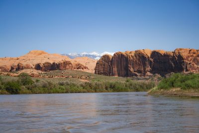 Silty spring flow on the Colorado River below Moab, with red slickrock domes on the right bank and the snow-capped La Sal Mountains on the horizon.