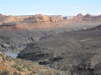 View from a rocky rim above Westwater Canyon, with the muddy Colorado River in a black-walled gorge below and rounded red sandstone domes and towers across the plateau.