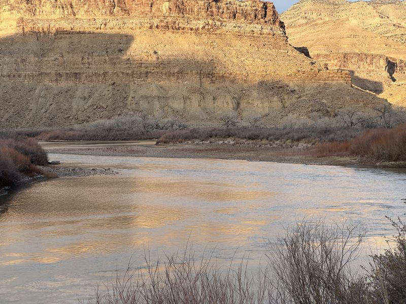 Low winter sun lights the layered tan cliffs of Gray Canyon above a calm bend of the Green River