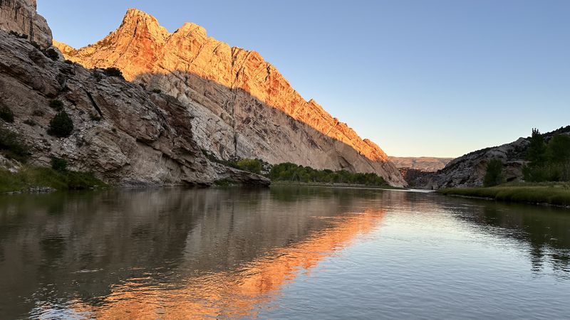 Last sunset light glows orange on the tilted sandstone cliffs of Split Mountain above a calm stretch of the Green River