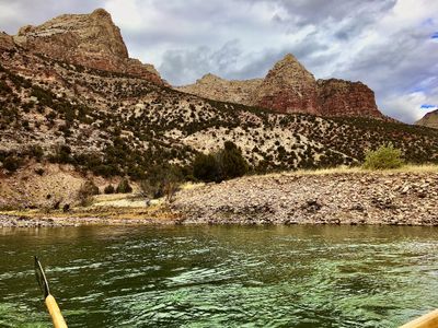 Storm clouds build over striped crag towers above a cobble bank of the Green River, with an oar blade skimming the green water in the lower left.