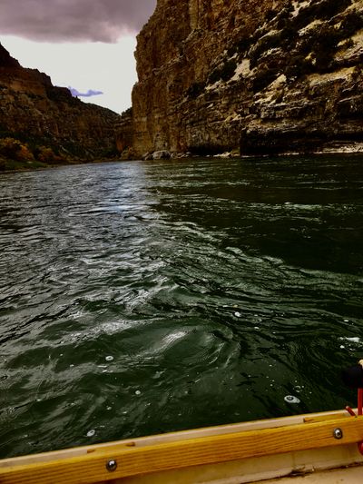 Dark green water and the wooden gunwale of a dory lead toward sheer canyon walls and a purple storm sky at the gates of Split Mountain Canyon.