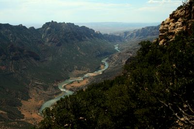 From high on the rim, Split Mountain Canyon opens in a deep V toward the hazy desert basin, with the Green River winding far below between pinnacled walls.