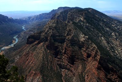 The folded rock flank of Split Mountain rises above the Green River, which S-curves through a green corridor far below, with hazy basin country in the distance.