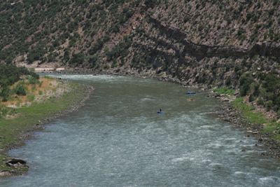 An oar raft and two inflatable kayaks spread out across a wide green stretch of the Green River, below juniper-covered slopes banded with ledgy rock.