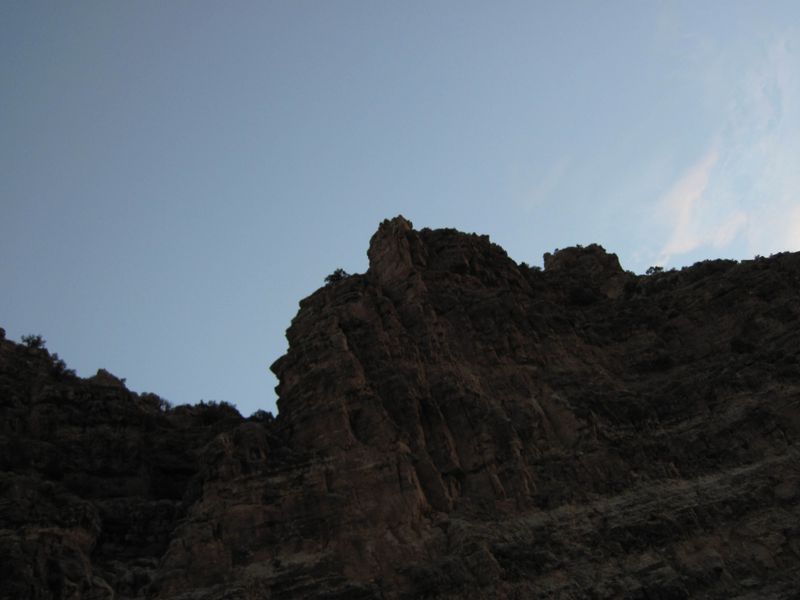 Twin rock pinnacles stand silhouetted on a craggy, juniper-dotted canyon rim against a pale evening sky above Whirlpool Canyon.