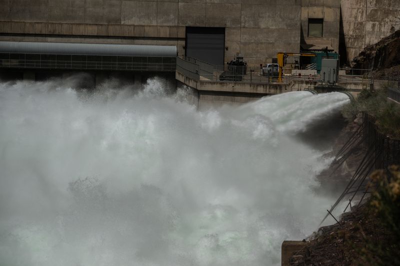 White water blasts from a jet tube at the base of a concrete dam and boils into a churning tailrace of spray and mist, with a service walkway