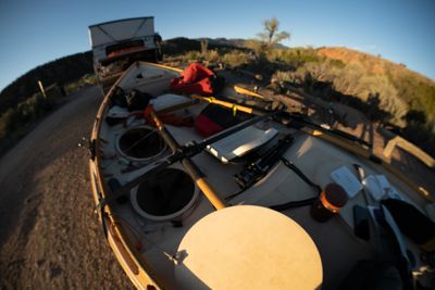 Fisheye view into a loaded wooden dory, oars and dry bags rigged at a dirt ramp at golden hour.