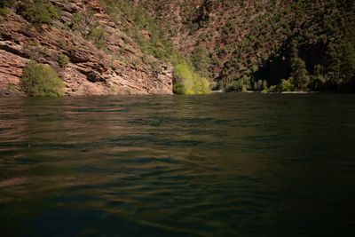 Green water fills the channel below a red rock ledge and juniper-dotted slopes.