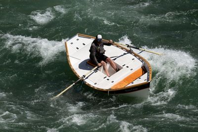 Overhead view of a rower working a white dory through churning water, a fishing rod along the deck.