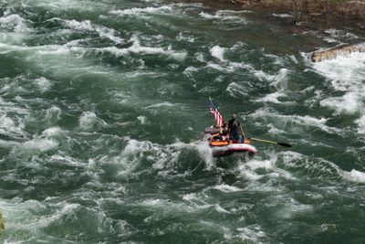 A loaded gear raft flying a small flag pushes through a wide field of whitewater, crew braced aboard.