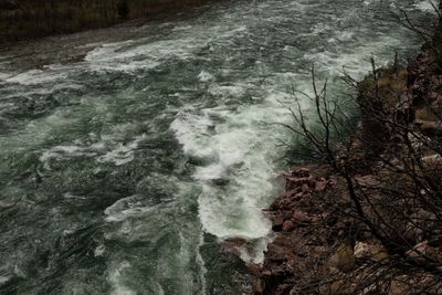 A train of white waves runs the length of the rapid past a bare-branched red bank.
