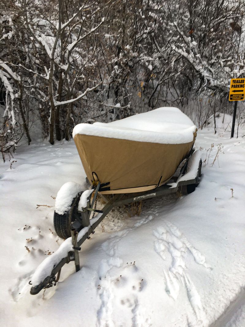 A dory sits on its trailer under a tan canvas cover buried in several inches of fresh snow