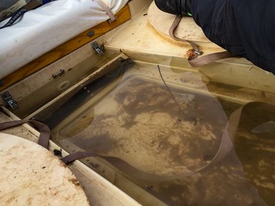 Muddy river water sloshes across the fiberglass floor and footwell of a dory, between strapped-down white bags, cam straps and a crew member's boot.