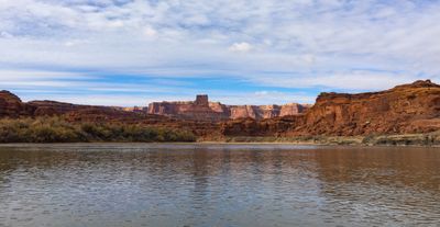 A wide view from river level of the brown river running between low red sandstone cliffs, with a squared sandstone tower on the skyline and a rippled sheet of altocumulus cloud filling the upper two-thirds of the frame.