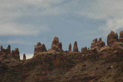 A skyline of banded sandstone spires, towers and rounded knobs standing along the canyon rim above Cataract Canyon, seen from river level under a hazy, partly clouded sky.