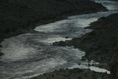 The Colorado River winding pale between dark canyon slopes at dusk, its banks, gravel bars and talus almost black in the failing light.