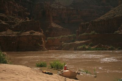 A wooden dory tied off on a sand beach beside muddy brown high water, with shadowed red canyon walls rising across the river.