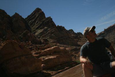 A crew member sits on the boat looking up at steep pointed sandstone ridges under a deep blue sky; the frame is motion-blurred and dark.