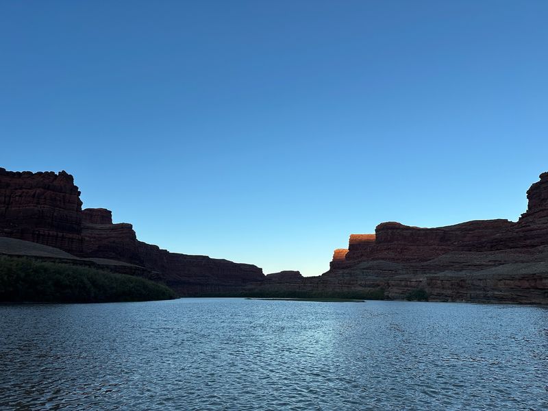 Wide, wind-rippled river filling the lower third of the frame between dark shadowed sandstone benches