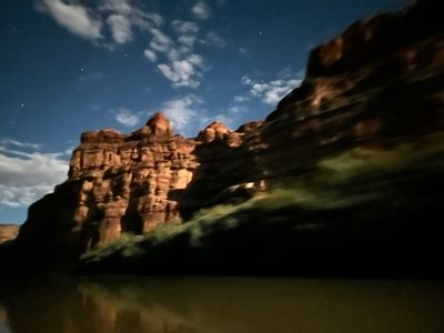 A moonlit sandstone cliff face glows warm against a deep blue night sky with scattered clouds and stars; the handheld long exposure has smeared the whole frame.