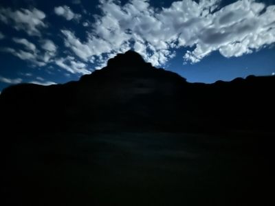 A butte and canyon skyline stand as a flat black silhouette against a moonlit, cloud-streaked deep blue night sky; the entire foreground is dark.