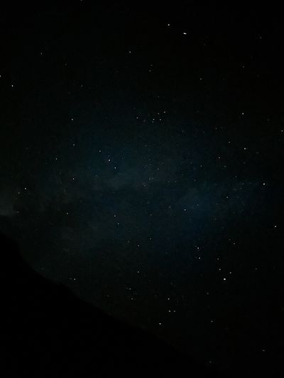 A dark night sky scattered with faint stars over the black silhouette of a canyon rim crossing the lower left corner of the frame.