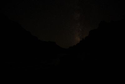 The Milky Way and a dense field of stars fill the sky above the black silhouette of canyon walls, with the foreground almost completely dark.