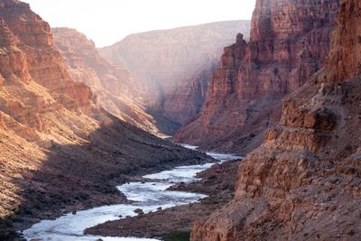 From high above, the river glints silver as it winds through a deep red-walled canyon, late sun and haze filling the gorge downstream.