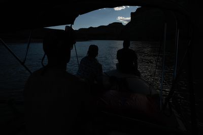 Three crew members silhouetted on a raft as the canyon fades to dusk.