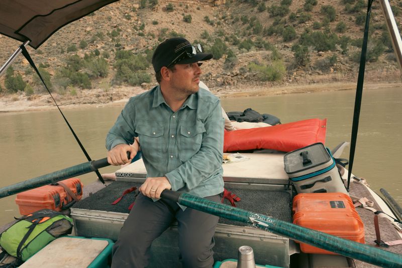 Oarsman rowing beneath a shade canopy as canyon walls rise on both sides of the river.