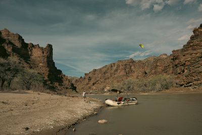 A loaded raft parked at the edge of a sandy beach with a kite in the air and canyon walls downstream.