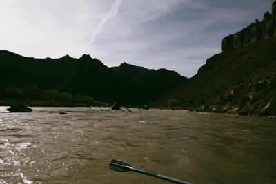 An oar blade dips into silty current as the river runs between dark, silhouetted canyon walls.